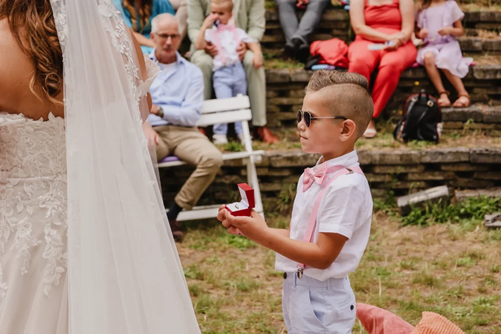 Bruidegom in wit overhemd houdt hand van bruid in trouwjurk vast tijdens ceremonie buiten