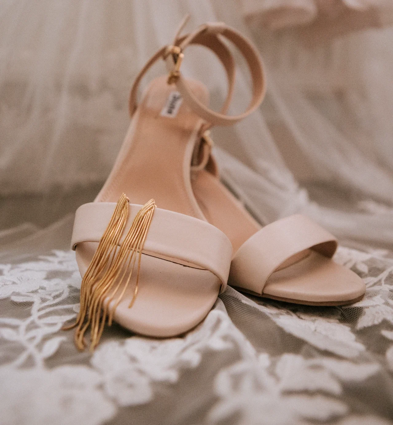 Elegante bruidsschoenen in crème met gouden franje en enkelbandje op kant bruidsstof.